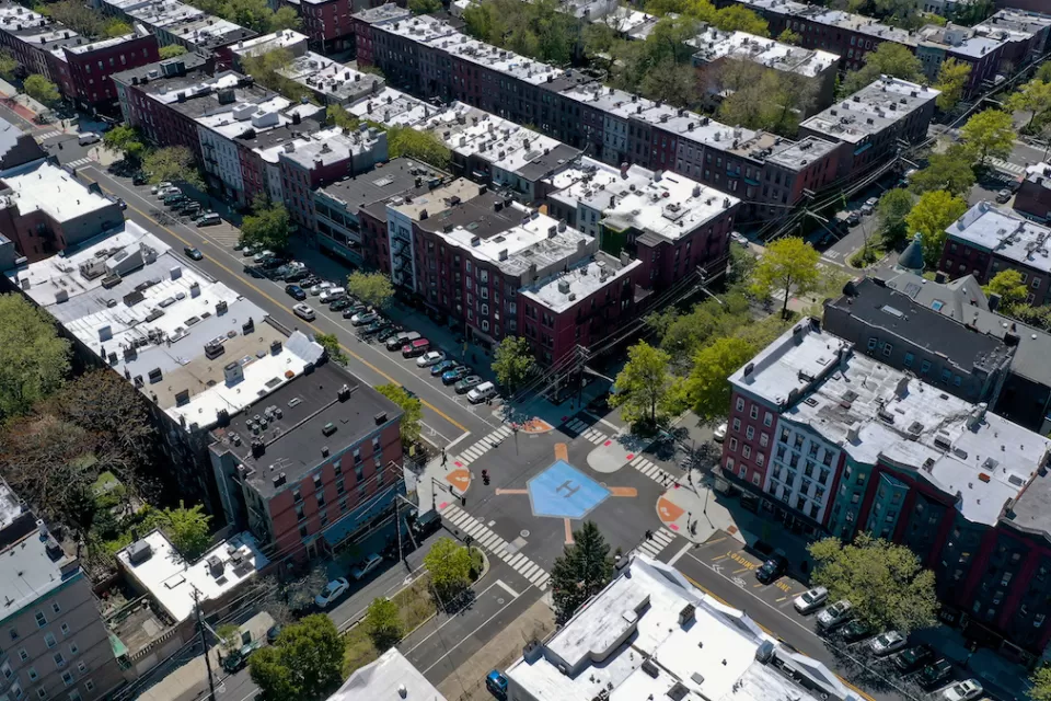Aerial view of intersection in Hoboken, New Jersey with crosswalks, bulb-outs, and blue home plate painted in middle of intersection, surrounded by mid-rise multistory apartment buildings.